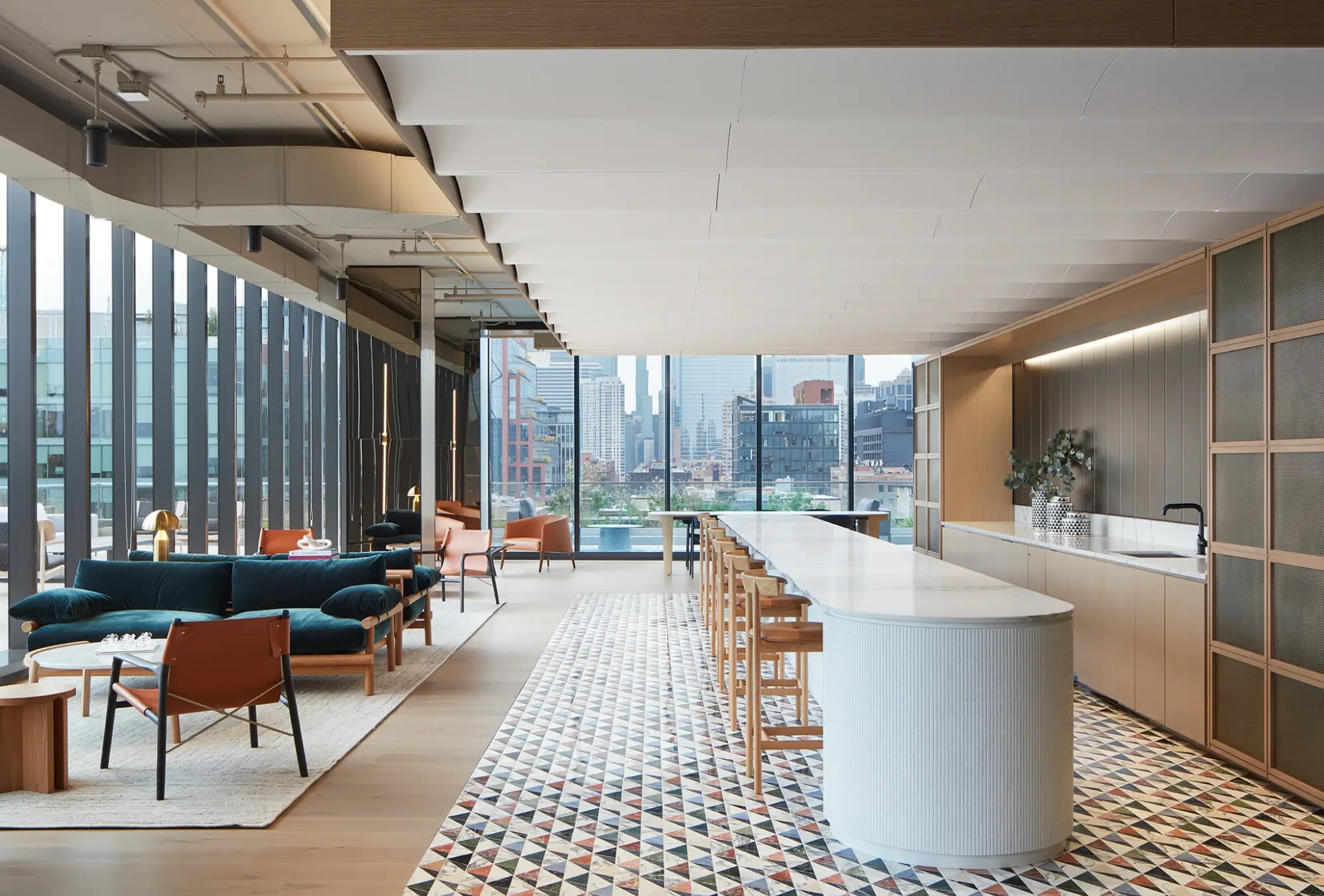 Sleek lounge and kitchen space with velvet seating, curved counter, and city views beyond windows