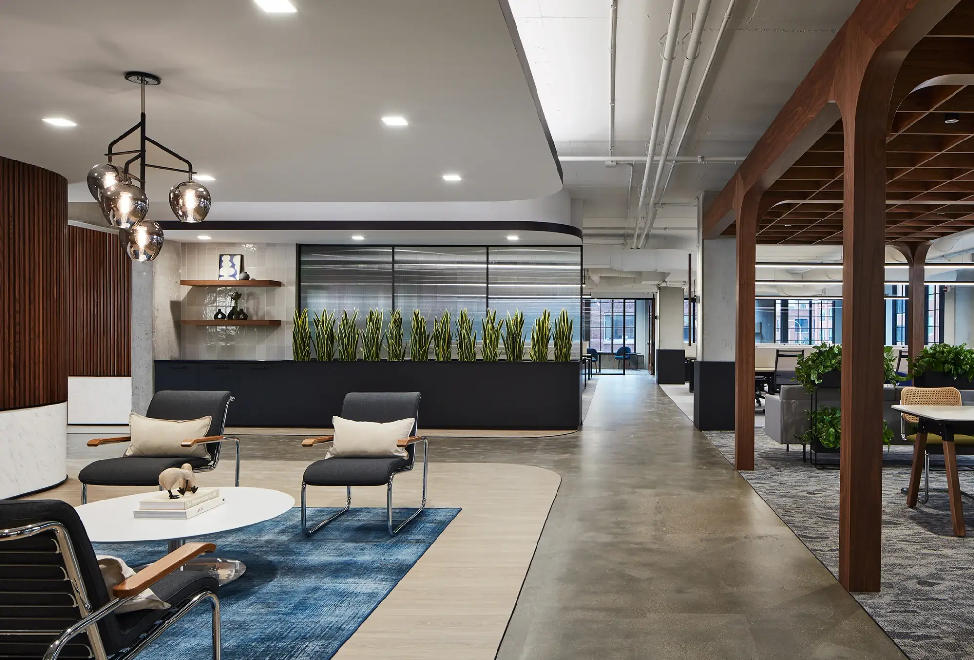 Open office lounge with structured ceiling, wood paneling, and indoor planters adding natural touches.