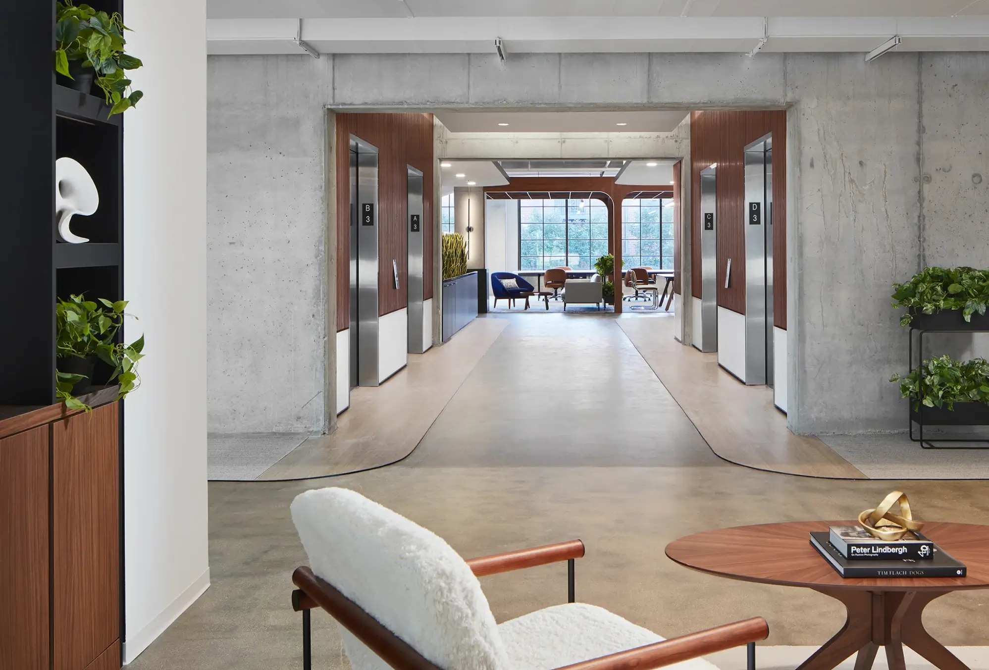 Hallway view of elevator banks with wood paneling and modern seating area beyond large windows