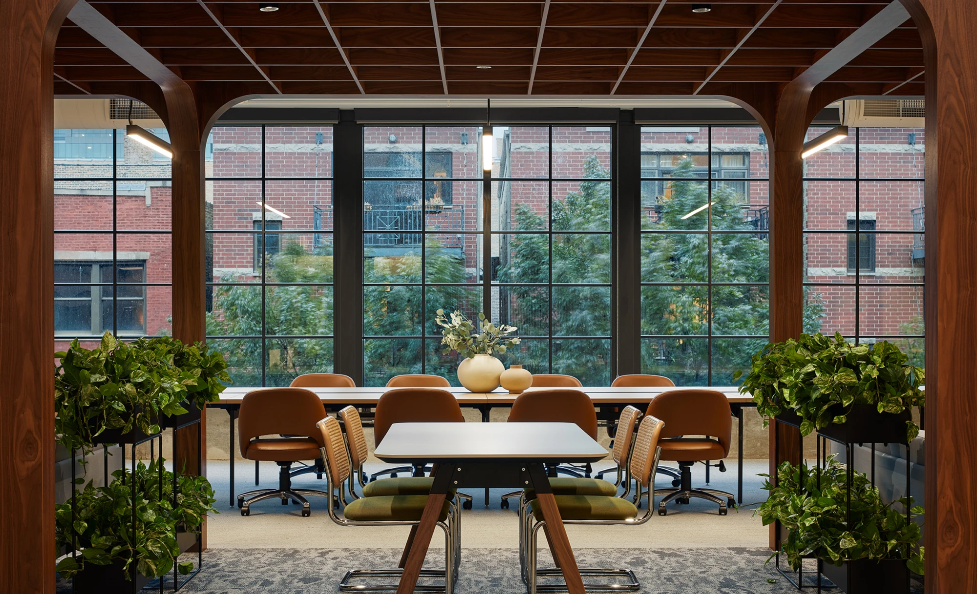 Lounge area with velvet seating, exposed ceilings, and panoramic windows overlooking city buildings